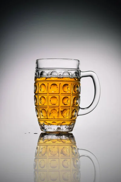 Verre avec bière froide légère en verre transparent sur surface réfléchissante grise — Photo de stock