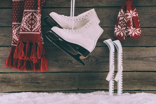 Bufanda roja con guantes y patines blancos colgados en la pared de madera - foto de stock