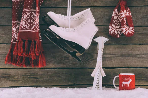 Red scarf with gloves and white skates hanging on striped wall — Stock Photo