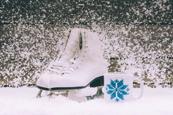 Pair of white skates with cup on snow — Stock Photo