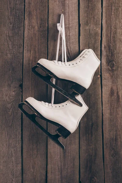 Pair of white skates hanging on wooden wall with shoelaces — Stock Photo