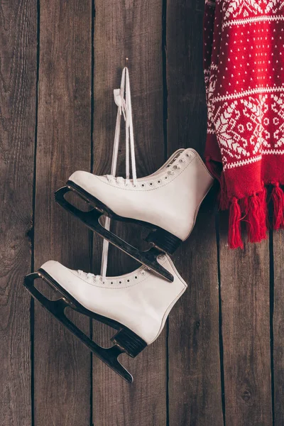 Pair of white skates and red scarf hanging on wooden wall — Stock Photo