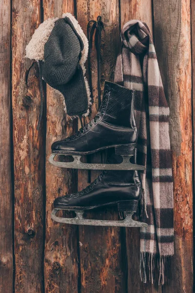 Hat with ear flaps with scarf and black skates hanging on wooden wall — Stock Photo