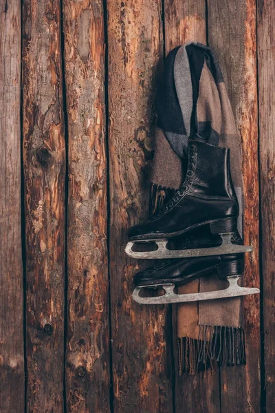 Warmer Schal mit schwarzen Schlittschuhen, die an der Holzwand hängen — Stockfoto