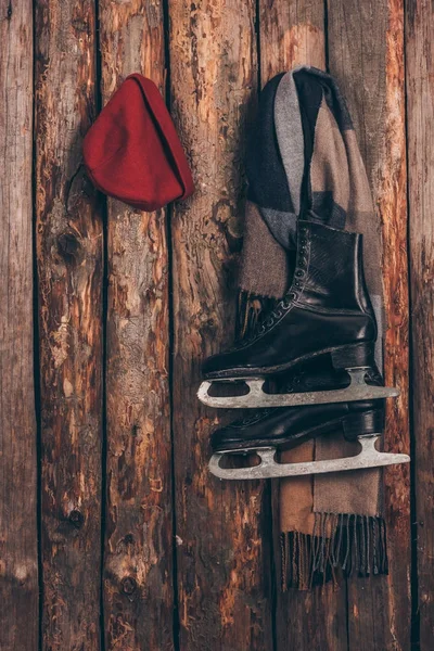 Red hat with scarf and black skates hanging on wooden wall — Stock Photo