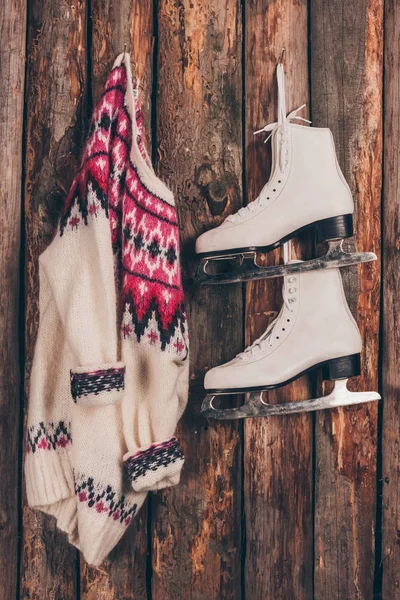 Теплый свитер и пара белых коньков висят на деревянной стене — стоковое фото