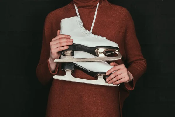Cropped image of woman in brown sweater holding skates isolated on black — Stock Photo