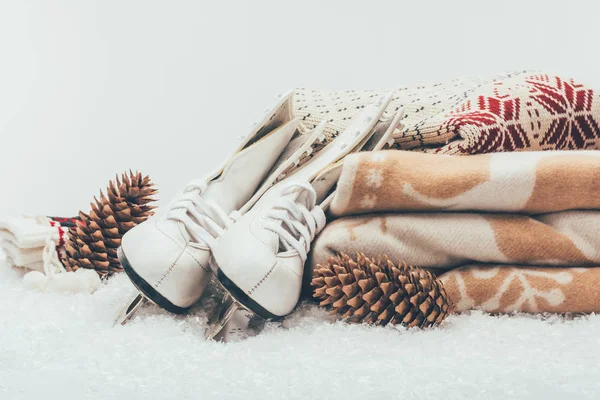 White skates with pine cones and stack of blanket and sweater — Stock Photo