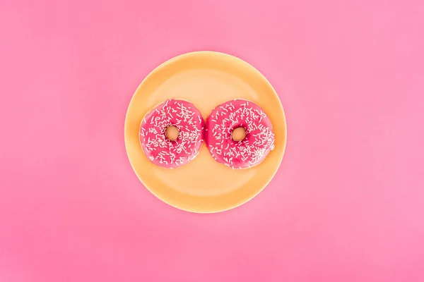 Vista superior de rosquillas acristaladas rosadas sobre placa amarilla aislada sobre rosado - foto de stock