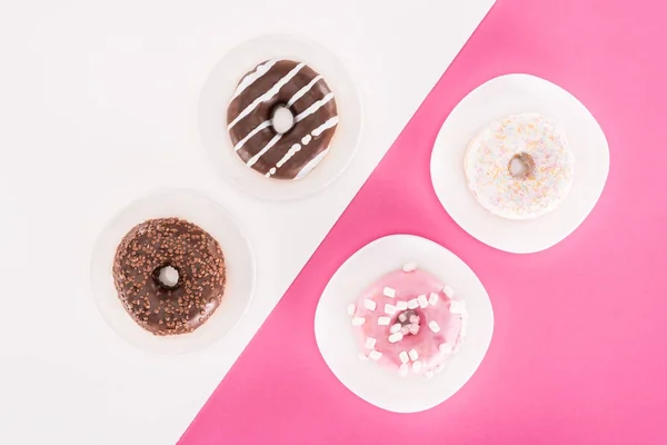 Вид сверху на различные вкусные пончики на тарелках — стоковое фото