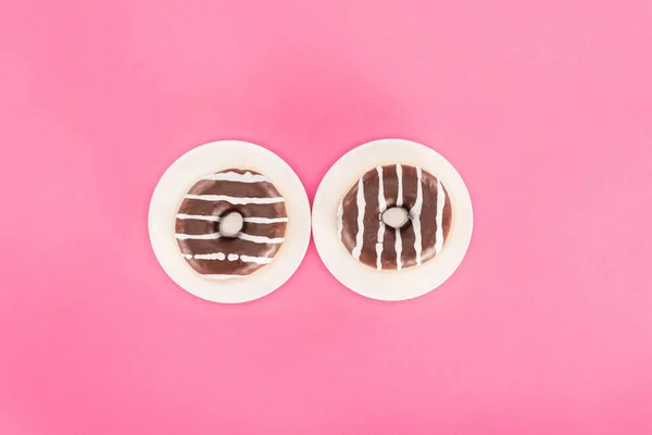 Верхний вид пончиков, остекленных шоколадом на тарелках, изолированных на розовый — стоковое фото