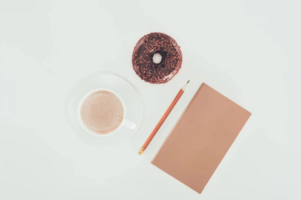 Vista superior de rosquilla acristalada con taza de café y papel kraft en blanco sobre mesa blanca - foto de stock