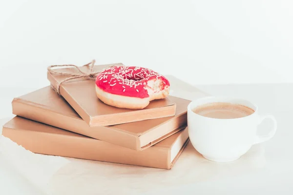 Delicioso donut rosa en libros apilados con taza de café - foto de stock