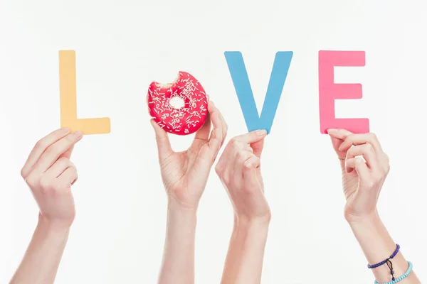 Tiro cortado de mulheres montando palavra de amor com letras coloridas e rosquinha mordida — Fotografia de Stock