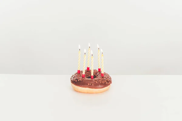 Delicioso donut glaseado con velas de cumpleaños en la mesa blanca - foto de stock