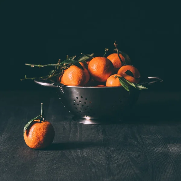 Close up view of pile of mandarins with leaves in strainer on dark wooden tabletop — Stock Photo