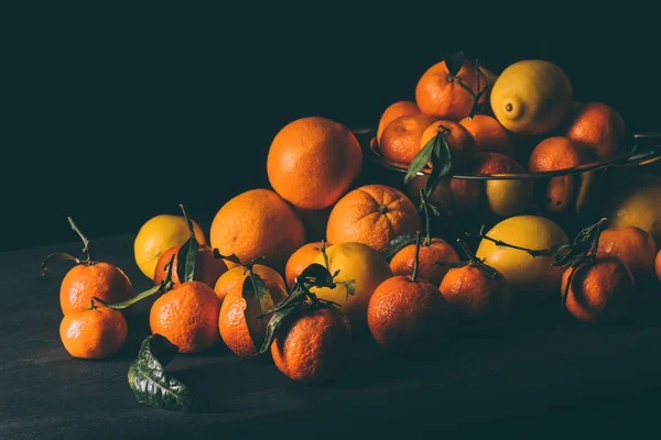 Primer plano vista de pila de limones y mandarinas con hojas en colador en la superficie oscura - foto de stock