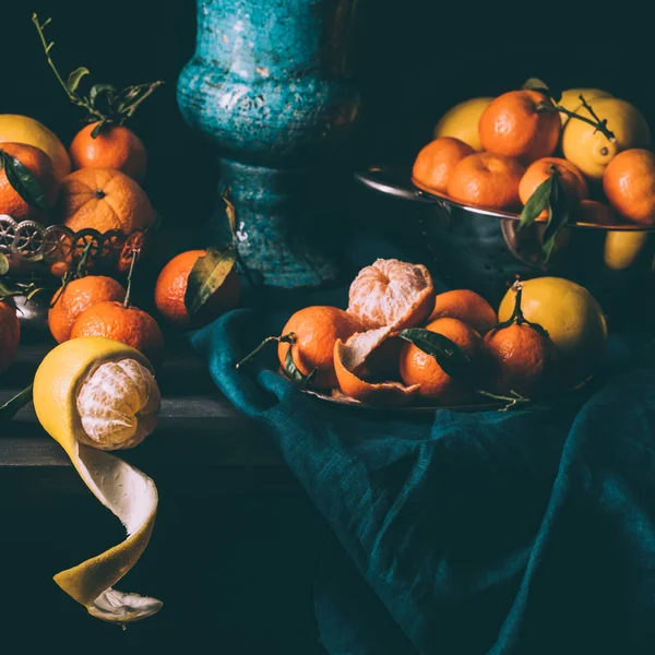 Close up view of arrangement of fresh lemons and tangerines in bowl and strainer on table with dark tablecloth — Stock Photo