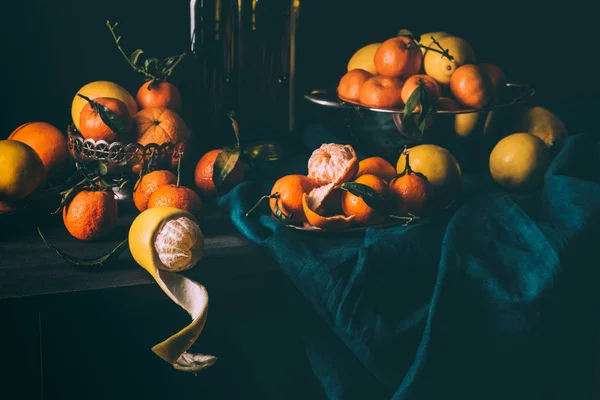 Vista ravvicinata della disposizione di limoni freschi e mandarini in ciotola e colino sul tavolo con tovaglia scura — Foto stock