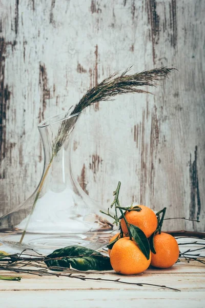 Vue rapprochée des mandarines sur une surface en bois pâle avec plante dans un vase à proximité — Photo de stock