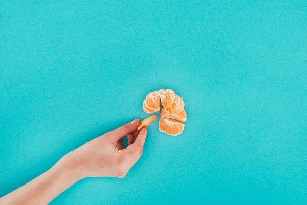 Vista parcial de la mano femenina y la mandarina aislada en azul - foto de stock