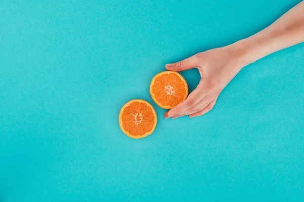 Partial view of woman holding piece of orange isolated on blue — Stock Photo