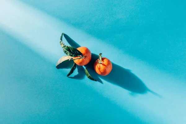 Vista superior de tangerinas dispostas com folhas na superfície azul — Fotografia de Stock