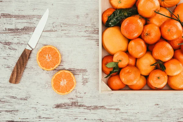 Flat lay with tangerines in box, pieces of orange and knife on shabby wooden tabletop — Stock Photo