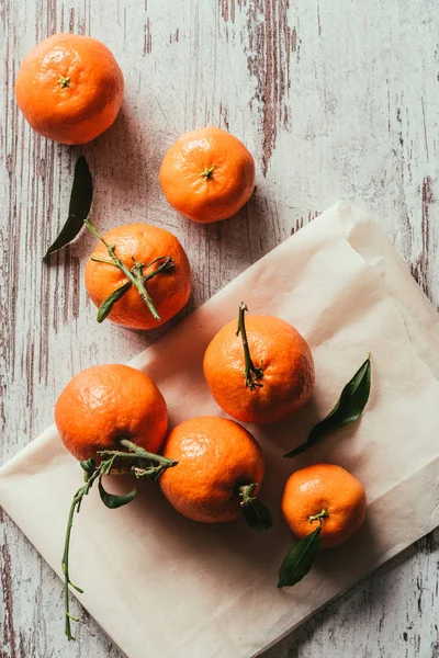 Vue de dessus des mandarines avec des feuilles sur papier cuisson sur plateau rustique — Photo de stock