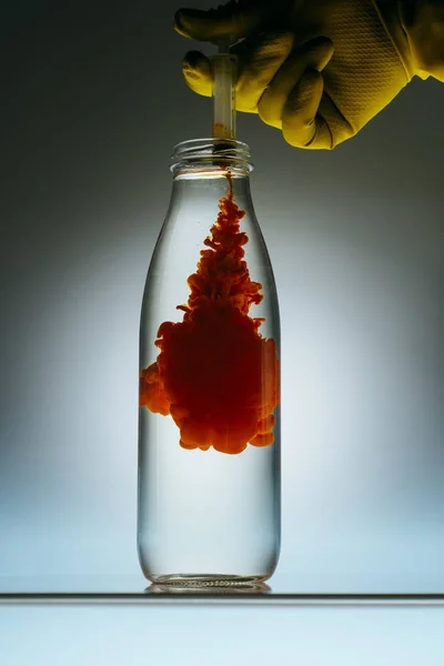 Cropped view of person pouring red paint from syringe into bottle with water — Stock Photo