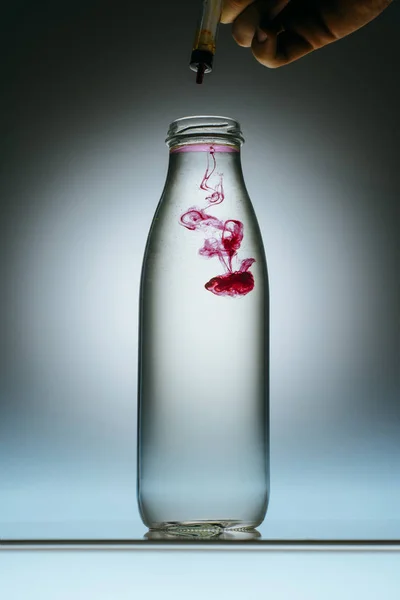 Ausgeschnittene Ansicht einer Person, die rosa Farbe in eine Flasche mit Wasser gießt — Stockfoto