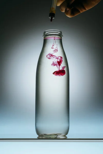 Cropped view of person pouring pink paint into bottle with water — Stock Photo