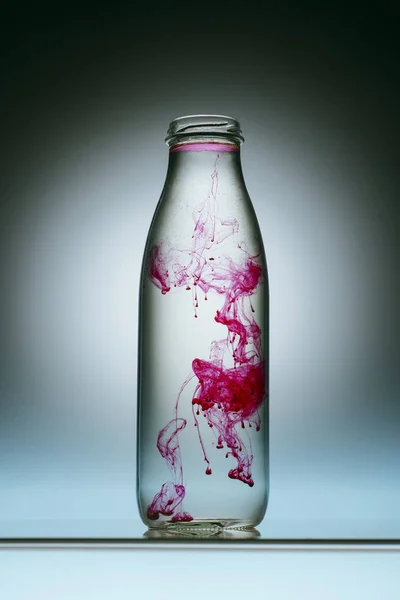 Close up view of pink paint splash in bottle of water — Stock Photo