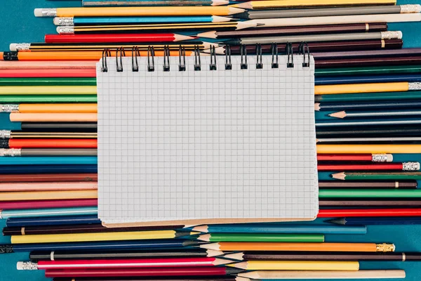 Vista superior de la composición de lápices de colores con cuaderno en blanco aislado sobre fondo azul - foto de stock