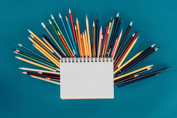 Vue du dessus de la composition de crayons colorés avec bloc-notes vierges isolés sur fond bleu — Photo de stock