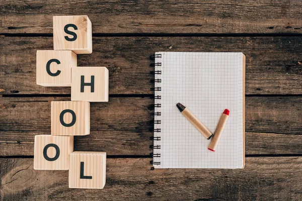 Ansicht der Zusammensetzung von Buntstiften mit leerem Notizbuch und Wortschule auf Holzgrund — Stockfoto