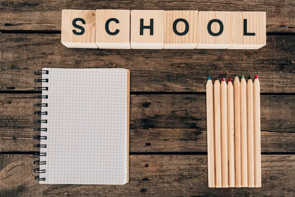 Vue du dessus de la composition de crayons colorés avec carnet vierge et école de mots sur fond en bois — Photo de stock