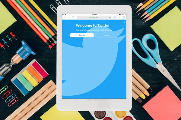 Tablette plate avec application Twitter sur fond avec fournitures scolaires isolées sur fond sombre — Photo de stock