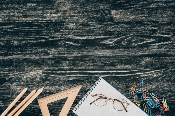 Vista dall'alto della composizione di colorati materiali scolastici con taccuino bianco sullo sfondo a bordo — Foto stock