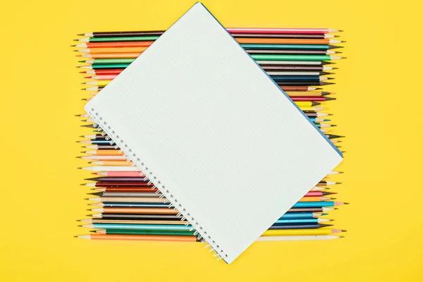 Вид зверху на композицію барвистих олівців з порожнім ноутбуком ізольовано на жовтому фоні — стокове фото