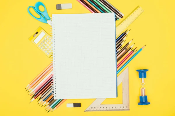 Vista superior de la composición de materiales escolares coloridos con cuaderno en blanco aislado sobre fondo amarillo - foto de stock