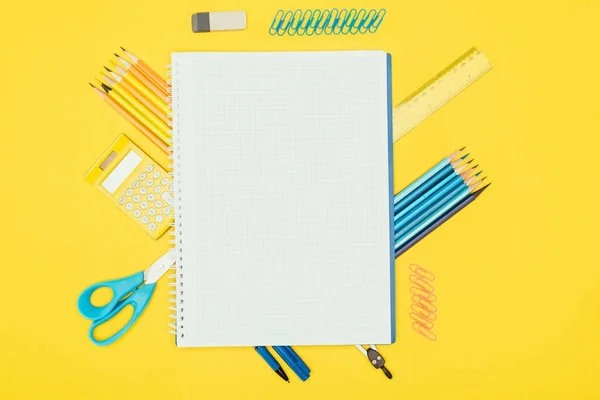 Vista superior de la composición de materiales escolares coloridos con cuaderno en blanco aislado sobre fondo amarillo - foto de stock