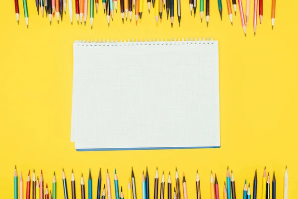 Top view of frame of colorful pencils isolated on yellow background with notebook — Stock Photo