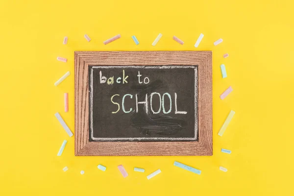 Top view of Back to school inscription on chalk board with chalks isolated on yellow — Stock Photo