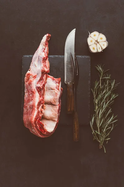 Top view of raw pork ribs on stone slate with cutlery and spices — Stock Photo