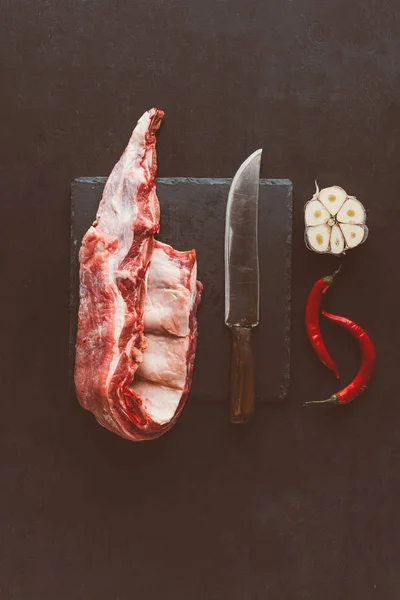 Vista superior de las costillas de cerdo crudo rebanada en pizarra de piedra con cuchillo y especias - foto de stock