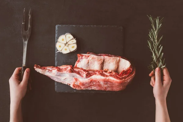 Tiro recortado de mujer con tenedor y costillas en bruto rebanada en pizarra de piedra - foto de stock