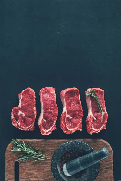 Vue du dessus des steaks crus en rangée avec des épices sur une planche en bois — Photo de stock