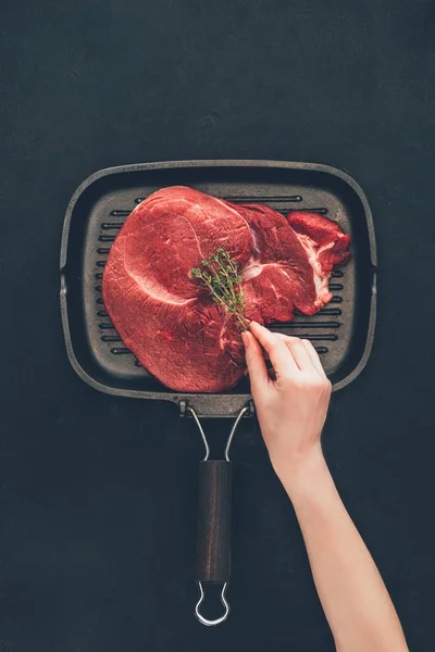 Tiro recortado de la mujer poniendo hierba en carne cruda en la parrilla - foto de stock