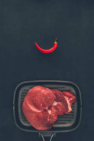 Top view of raw steak on grill pan with chili pepper — Stock Photo